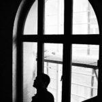 Black and white silhouette of a man standing by an arched window, creating a contemplative mood.